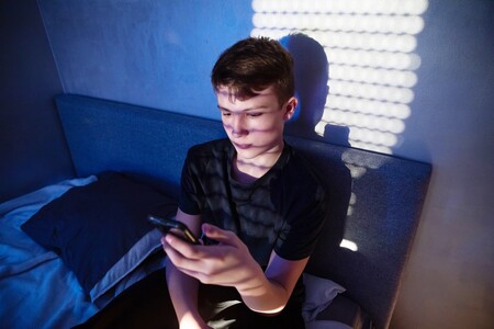 Ein Junge sitzt auf seinem Bett und schaut ernst auf sein Handy.