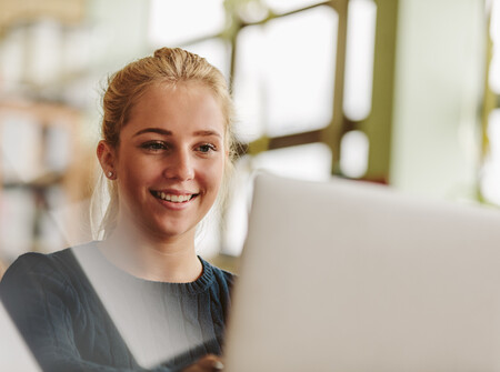 Eine junge Frau sitzt vor ihrem Laptop und lächelt.