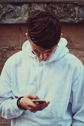 Junger Mann in weißem Pullover guckt auf sein Smartphone.