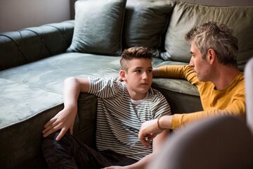Ein Vater und Sohn im ernsten, aber zugewandten Gespräch im Wohnzimmer.