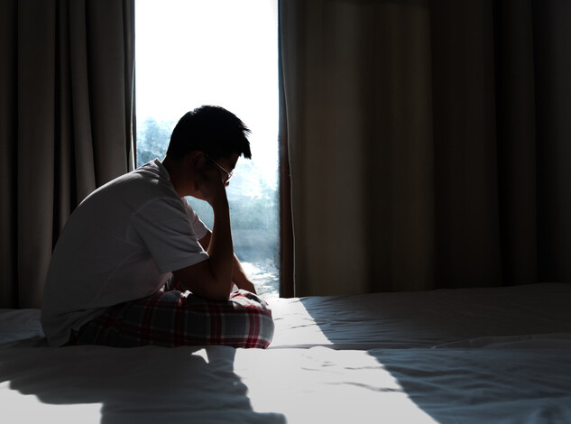 Ein Junge sitzt traurig auf dem Bett, es ist dunkel.