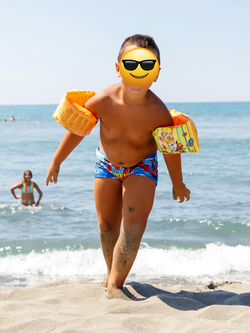 Ein Emoji reicht oft nicht aus, um die Identität eines Kindes zu schützen. Das Bild zeigt einen Jungen, der am Strand direkt vorm Meer steht und ein Emoji mit Sonnenbrille in seinem Gesicht platziert hat.