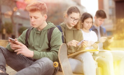 Vier Schülerinnen und Schüler sitzen in der Pause nebeneinander, jeder schaut auf sein Handy.