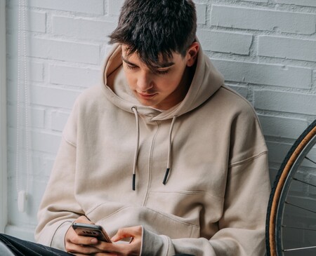 Erkennen von Kettenbriefen und Handlungsempfehlungen Ein Junge sitzt an eine Wand gelehnt und schaut auf sein Handy.