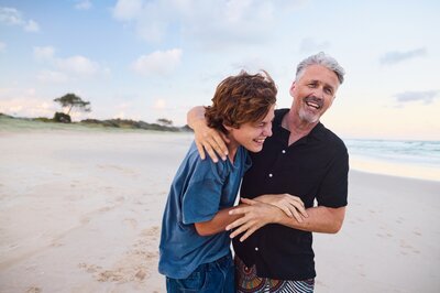 Vater und Sohn Vater und Sohn umarmen sich am Strand und lachen.