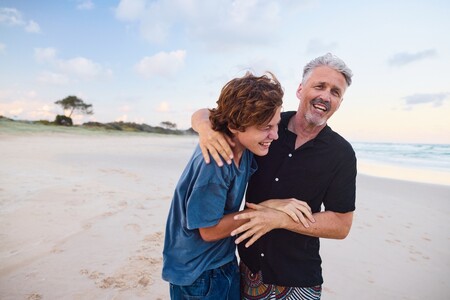 Vater und Sohn umarmen sich am Strand und lachen.