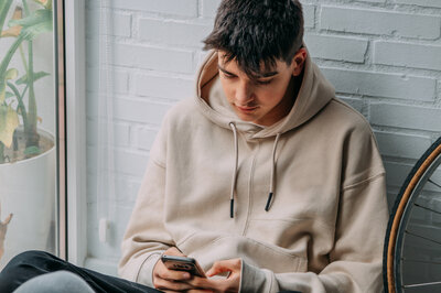 Cybermobbing ist strafbar und sollte daher immer gemeldet werden. Zu sehen ist ein Jugendlicher, der auf sein Handy schaut.