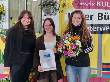 Medienpädadogin Ann-Kristin Gaumann und die JUUUPORT-Scoutinnen Charlotte und Charlotte haben den Kinder-Online-Preis auf der Leipziger Buchmesse entgegen genommen. Drei Personen stehen mit der Auszeichnung und einem Blumenstrauß nebeneinander und lächeln in die Kamera.