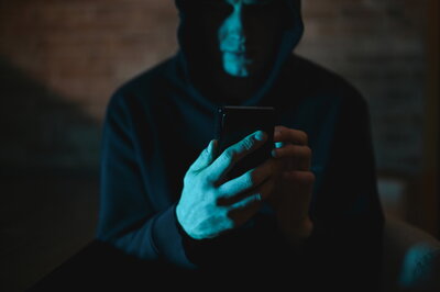 Cybergrooming Ein Mann schaut im Dunkeln auf sein Handy. Er trägt eine Kapuze.