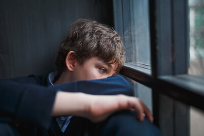 Ein Junge schaut traurig aus dem Fenster.