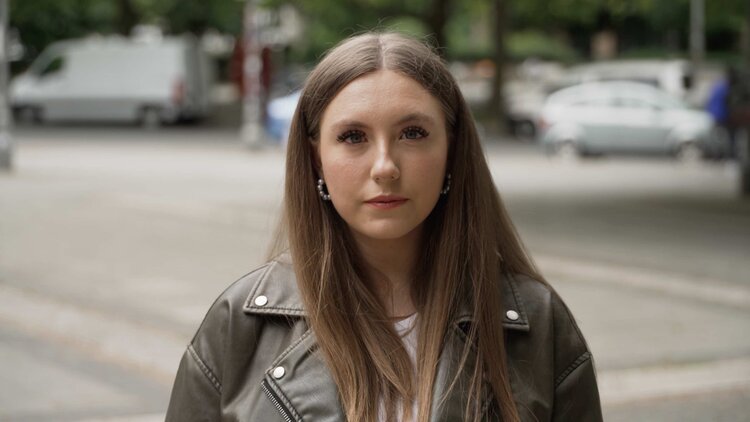 Eine junge Frau namens Celine schaut ernst in die Kamera.