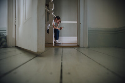 Junge sitzt auf einer Treppe und schaut traurig auf sein Smartphone