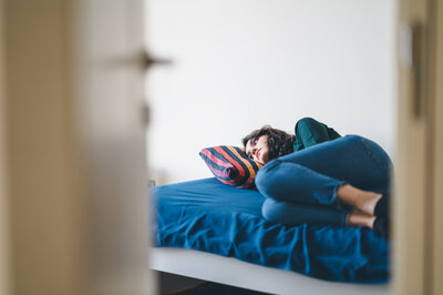 Eine junge Frau liegt traurig in ihrem Zimmer auf dem Bett.