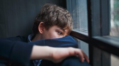 Ein Junge schaut traurig aus dem Fenster