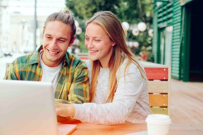 Ein junger Mann und eine junge Frau sitzen lächelnd vor einem Laptop