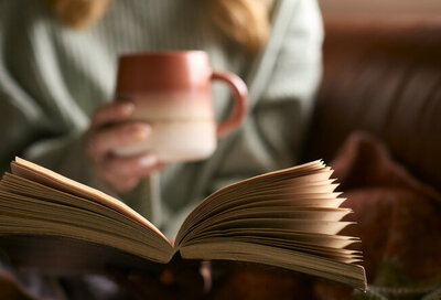 Eine junge Frau liest ein Buch und hält eine Tasse Tee in der Hand