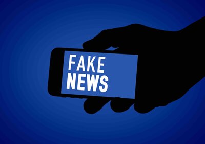 Handy in der Hand, auf dem Display steht Fake News