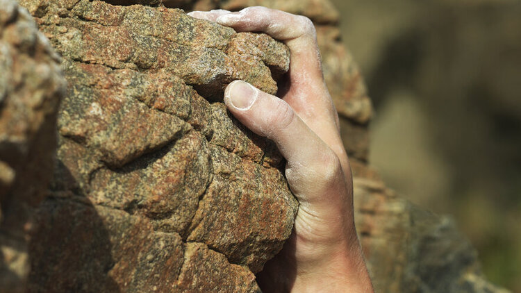 Eine Person hält sich mit einer Hand an einem Felsen fest.