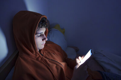 Teenager mit kapuzenpullover, der im Dunkeln auf sein Smartphone schaut.