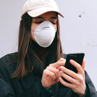 Coronavirus: Smartphone desinfizieren? Mädchen mit Maske hält Smartphone in den Händen