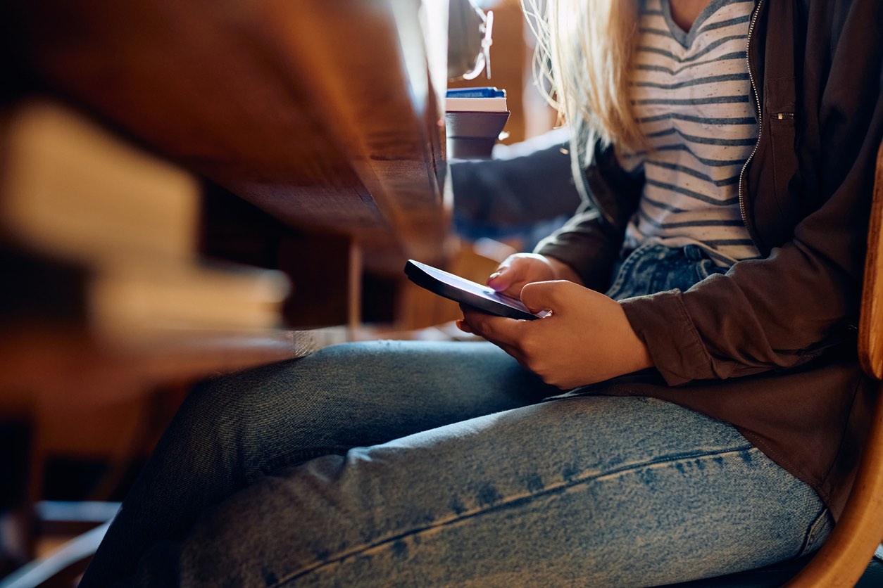 Eine Schülerin schaut unter dem Tisch heimlich auf ihr Handy.